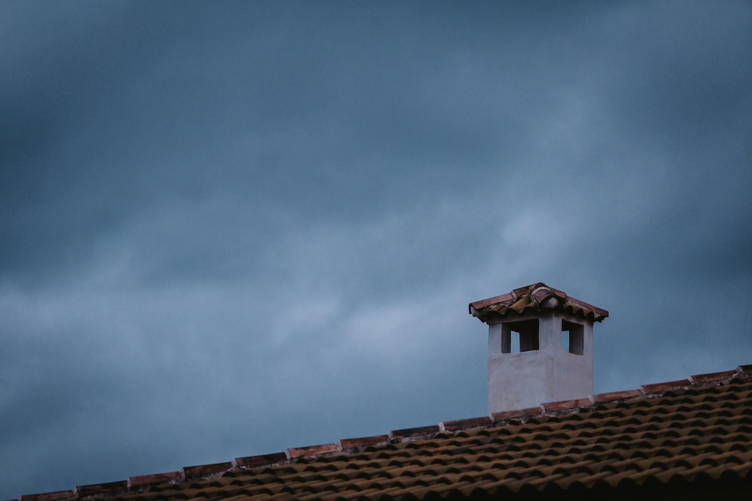 A rooftop chimney with tiled roof under a dramatic cloudy sky during twilight.
