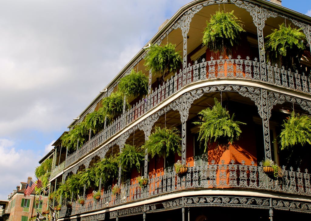 Detailed view of ornate ironwork balconies with lush greenery in New Orleans under a vibrant sky.
