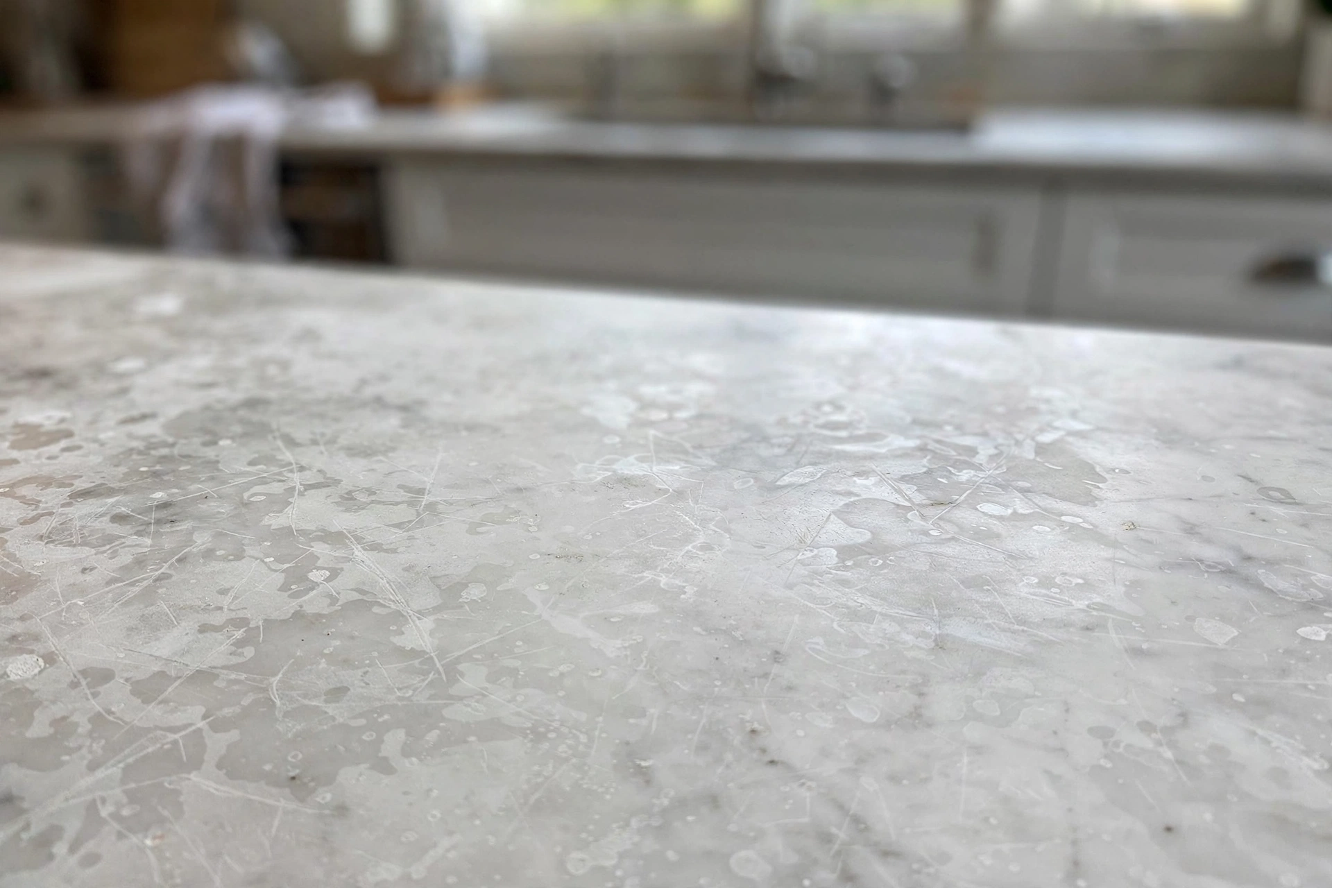 Close-up of a dull, etched marble countertop with visible etch marks and water spots
